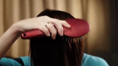 Tanınmayan bir kadın ıslak saçlarını bir tarakla tarıyor. Yakın plan. Saç bakımı. Koyu arkaplan.