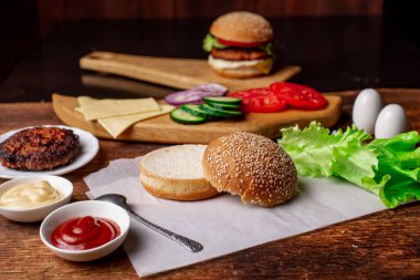 Klasik bir hamburger için gerekli malzemeler. Izgara et, sebze, sebze, susamlı ekmeğin yanında soslar. Ahşap arka plan. Hamburger mi çizburger mi?.