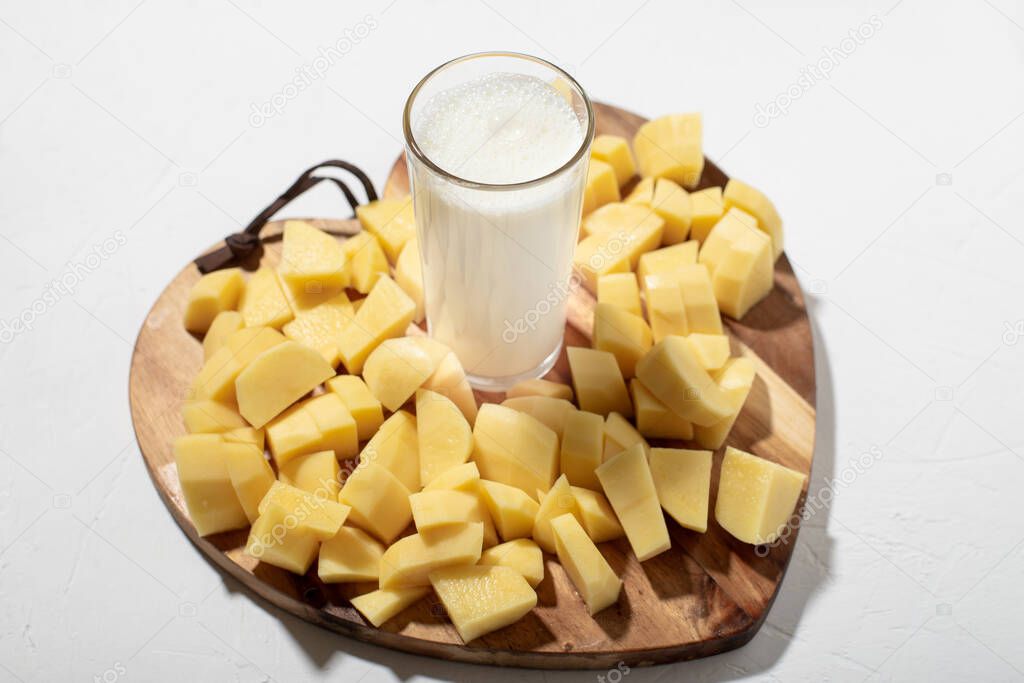Potato milk concept. Alternative milk. A glass of milk on a wooden board with chopped raw potatoes.