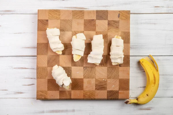 用香蕉煮羊角面包 用生面团包香蕉 轻型木制背景 在笼中切板 — 图库照片