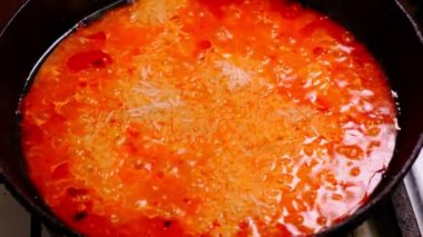 Jollof pilav pişirme. Domates ezmeli pilav, domates, baharat bir tavada pişirilir. Spatula hareketi.