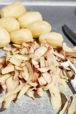 Çiğ patates soymak. Masada bir sürü kabuk ve soyulmuş patates var. Dikey oryantasyon. Yemek hazırlığı.