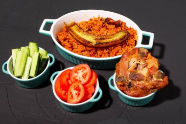 Kızarmış muzlu jollof pilav, fırında tavuk. Domatesli pilav, soğan, baharat. Geleneksel Nijerya yemekleri. Koyu arkaplan.