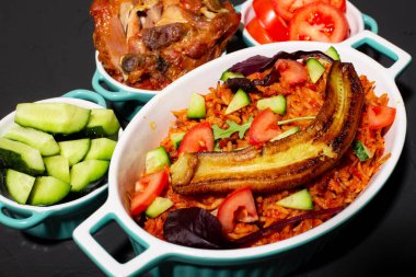 Kızarmış muzlu jollof pilav, fırında tavuk. Domatesli pilav, soğan, baharat. Geleneksel Nijerya yemekleri. Koyu arkaplan.
