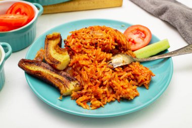 Jollof rice with fried banana on a plate. Rice with tomatoes, onions, spices. Fresh vegetables. White background. clipart