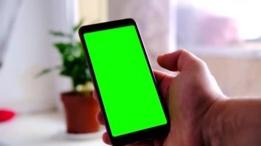 Oturma odasında yeşil ekranlı bir cep telefonu tutan bir el..