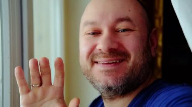 Orta yaşlı bir adam el sallıyor ve kameraya konuşuyor. Video çağrısı, çevrimiçi iletişim, blog yazma kavramı.