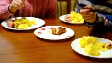 Birkaç tanınmayan çocuk sosis ve patates yiyor. Üç çocuklu yemek masası. Akşam yemeği..