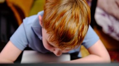 Evde eğitim. Karantinaya alın. Genç bir çocuk masada tek başına meşgul. Bir ilkokul öğrencisi bir not defterine kalemle yazar..