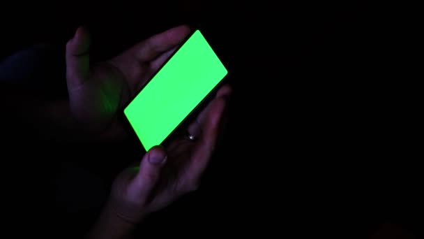 在黑暗中 男性的手拿着带有绿色屏风的手机 — 图库视频影像