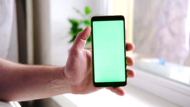 男の手はリビングルームで緑色の画面を持つショーの携帯電話を保持している — ストック動画