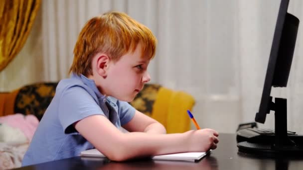 若い男の子は宿題をし 遠隔で勉強し コンピュータ画面の前にノートブックに書き込みます 家庭教育 — ストック動画