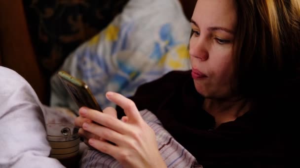 ソファに横になっていると 中年の女性が電話を見ている 魅力的な女性の40歳の嘘でベッド — ストック動画