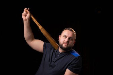 Genç bir adam ahşap bir sopa tutuyor. Fedai, güvenlik görevlisi, koruma konsepti. Tişörtlü iri bir adam kameraya bakar..