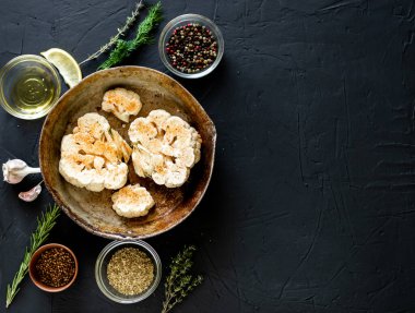 Karnabahar bifteği pişirme. Kızartma tavasına baharat serpiştirilmiş çiğ karnabahar. Zeytinyağı, bitkiler, yakınlarda çeşitli baharatlar. Karanlık arka plan. Kopyalama alanı.