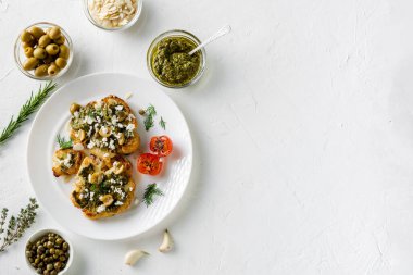 Baharatlı karnabahar bifteği, chimichurri sosu, badem gevreği, zeytin, kızarmış vişneli domates ve beyaz tabakta kapari. Vejetaryen yemeği. Beyaz arka plan. Kopyalama alanı.