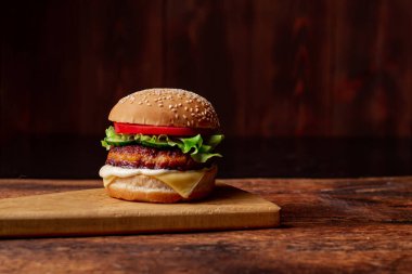 Kızarmış peynirli hamburger, yeşil salata ve domates. Ahşap arka plan. Hamburger Günü.