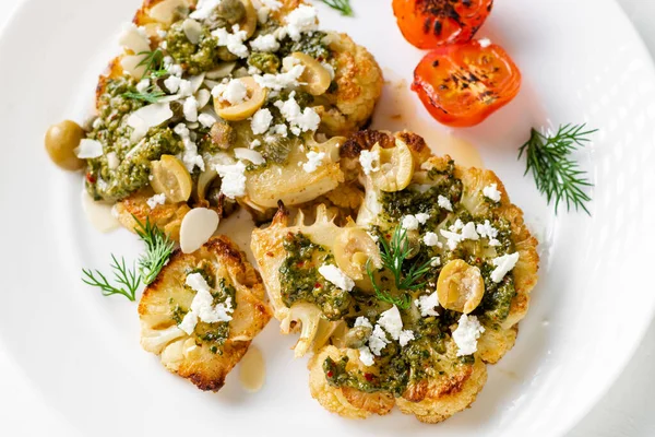 Baharatlı karnabahar bifteği, chimichurri sosu, badem gevreği, zeytin, kızarmış vişneli domates ve beyaz tabakta kapari. Vejetaryen yemeği..