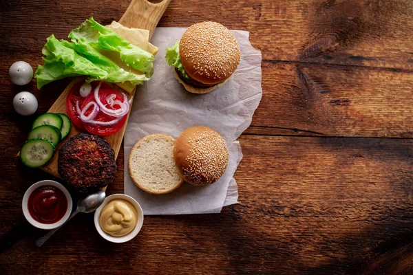 Hamburger ya da çizburger pişirmek. Klasik bir hamburger için farklı malzemeler. Mesaj için yer. Ahşap arka plan. Hamburger günü..