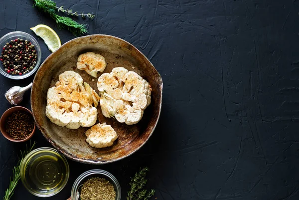 Karnabahar bifteği pişirme. Kızartma tavasına baharat serpiştirilmiş çiğ karnabahar. Zeytinyağı, bitkiler, yakınlarda çeşitli baharatlar. Karanlık arka plan. Kopyalama alanı.