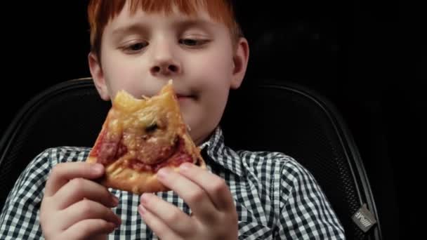 少年はピザを噛んだ 接近中だ 暗い背景 赤髪の少年 飢え食欲 — ストック動画