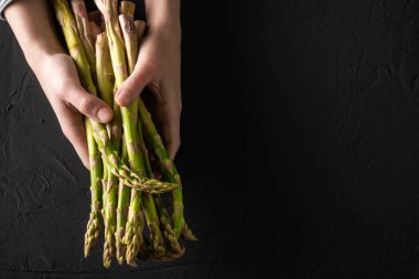 Kadın ellerinde kuşkonmaz sapları. Karanlık arka plan. Vejetaryenlik kavramı, sağlıklı beslenme..