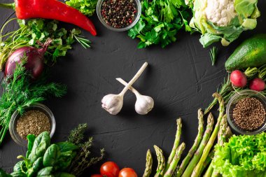 Farklı sebzeler. Ortaya iki diş sarımsak. Karanlık arka plan. Çerçeve. Vejetaryen yemeği. Sarımsağın faydaları.