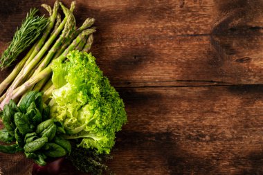 Ahşap arka planda çeşitli sebzeler. Marul, ıspanak, kuşkonmaz, biberiye. Vejetaryen gıda konsepti. Mesaj için yer. Yukarıdan görüntüle.