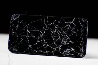 Siyah beyaz arka planda kırılmış bir cep telefonu. Telefonun siyah dokunmatik ekranında birçok çatlak var. Onarım, ekran değiştirme kavramı.