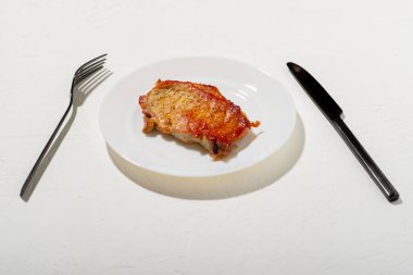 Beyaz tabakta bir parça kızarmış et. Siyah bıçak ve çatal. Kötü yağlı yemek. Beyaz arka plan. Diyet keto kavramı.