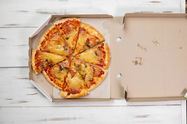 Pizza in a cardboard box. white wood background. Food concept. View from above.