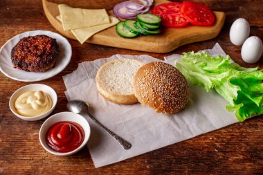 Klasik bir hamburger için gerekli malzemeler. Izgara et, sebze, sebze, susamlı ekmeğin yanında soslar. Ahşap arka plan. Hamburger mi çizburger mi?.