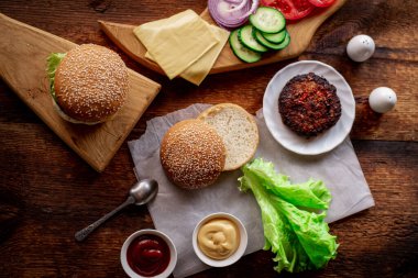 Hamburger günü. Hamburger ya da çizburger pişirmek. Klasik bir hamburger için farklı malzemeler. Mesaj için yer. Ahşap arkaplan.