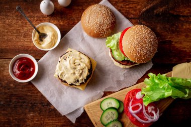 Hamburger ve çizburger için malzemeler. Ahşap arka plan. Hamburger sosla kaplı. Yemek pişirmek. Hamburger günü..
