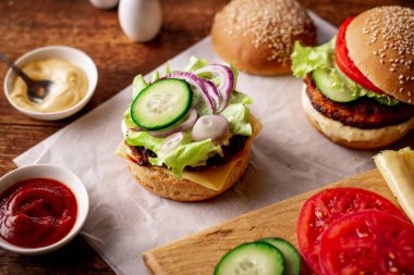 Hamburger pişiriyorum. Hamberger 'da sebze istiflemek. Ahşap arka planda farklı malzemeler var. Hamburger günü..
