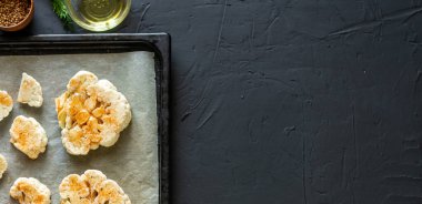 Karnabahar bifteği pişirme. Fırın örtüsünün üzerine baharat serpiştirilmiş çiğ karnabahar. Zeytinyağı, bitkiler, yakınlarda çeşitli baharatlar. Karanlık arka plan. Kopyalama. Pankart.