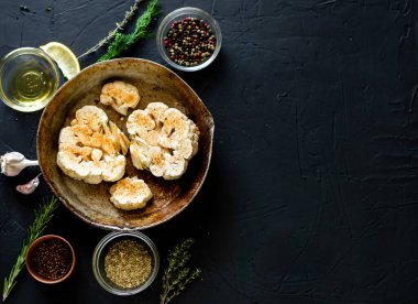 Karnabahar bifteği pişirme. Kızartma tavasına baharat serpiştirilmiş çiğ karnabahar. Zeytinyağı, bitkiler, yakınlarda çeşitli baharatlar. Karanlık arka plan. Kopyalama alanı.