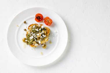 Baharatlı karnabahar bifteği, chimichurri sosu, badem gevreği, zeytin, kızarmış vişneli domates ve beyaz tabakta kapari. Vejetaryen yemeği..