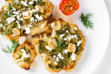 Baharatlı karnabahar bifteği, chimichurri sosu, badem gevreği, zeytin, kızarmış vişneli domates ve beyaz tabakta kapari. Vejetaryen yemeği..