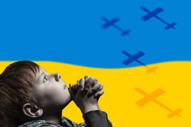 Bir çocuk Ukrayna bayrağının arka planında dua ediyor. Rus saldırganlığı. Uçan uçaklar.