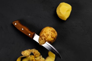 Patates ve bıçak. Patates soymak. Karanlık arka plan. Patates pişirmeye hazırlanıyorum..