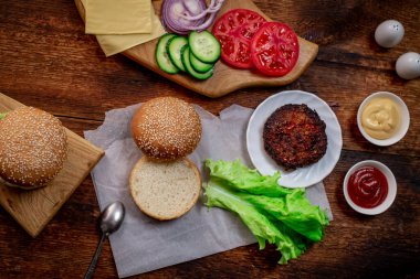 Hamburger ya da çizburger pişirmek. Klasik bir hamburger için farklı malzemeler. Izgara et, sebze, sebze, susamlı ekmeğin yanında soslar. Ahşap arka plan. Hamburger günü..