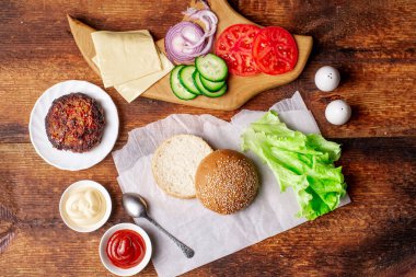 Klasik bir hamburger için gerekli malzemeler. Izgara et, sebze, sebze, susamlı ekmeğin yanında soslar. Ahşap arka plan. Hamburger mi çizburger mi?.
