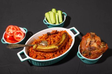 Kızarmış muzlu jollof pilav, fırında tavuk. Domatesli pilav, soğan, baharat. Geleneksel Nijerya yemekleri. Koyu arkaplan.