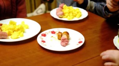 Birkaç tanınmayan çocuk sosis ve patates yiyor. Üç çocuklu yemek masası. Akşam yemeği..