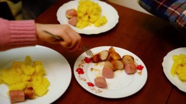Birkaç tanınmayan çocuk sosis ve patates yiyor. Üç çocuklu yemek masası. Akşam yemeği..
