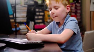 Genç bir çocuk bilgisayar başında ders çalışıyor ve evdeki bir deftere yazıyor. Ev, uzaklık öğrenme.