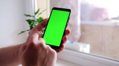 Erkek eller yeşil ekranlı bir cep telefonu tutuyor. Parmağını onun üzerinde gezdiriyor. Yanlış anlama jesti, hayal kırıklığı.