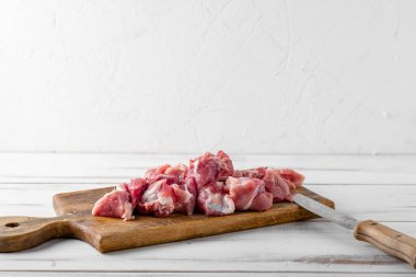 Dilimlenmiş çiğ et parçaları beyaz ahşap arka planda bir kesme tahtasının üzerinde. Domuz eti ya da sığır eti pişirmeye hazır..