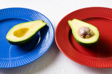 Avokadoyu mavi ve kırmızı tabakta kes. Beyaz arka plan. Minimalizm. Sağlıklı gıda konsepti.